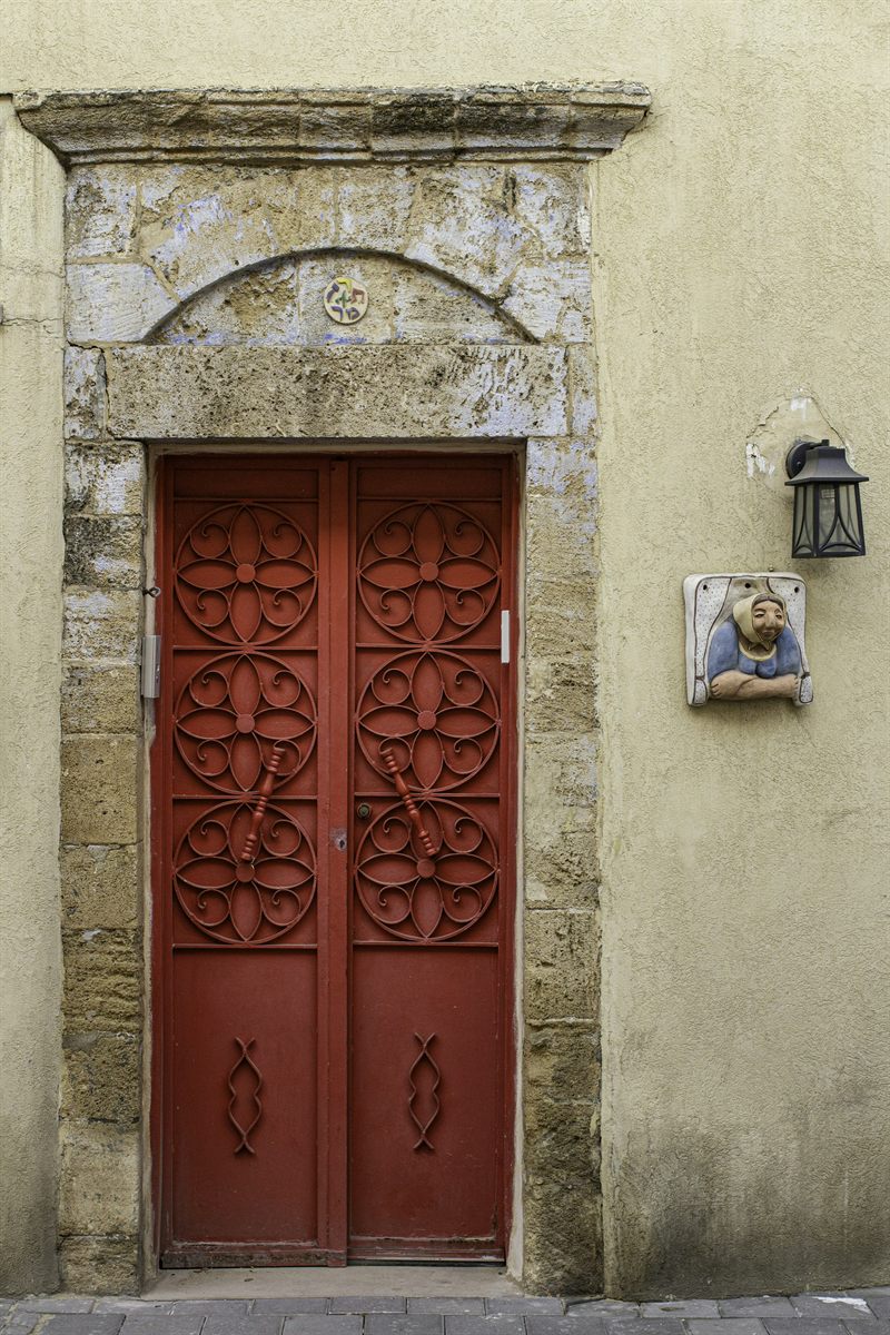 An old red wooden door with ornaments in a pale stone facade in Neve Tzedek, Tel Aviv