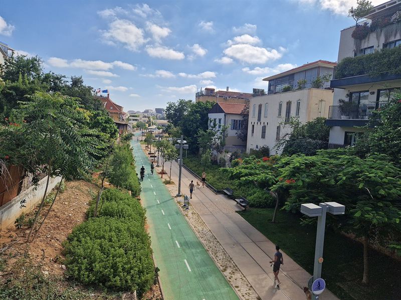 Park HaMesila von der Shlush-Brücke aus: ein Weg mit alten Schienen, Radweg, Bäume und die Häuser von Neve Tzedek